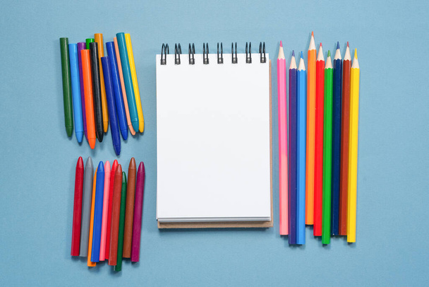 Colorful pencils and blank paper page with copy space on blue background. - Foto, imagen