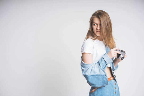 Cute girl on white background copy space in photo Studio. Holds a retro camera. Wearing a denim suit. Denim long skirt and jacket. Nostalgia 90's. - Photo, Image