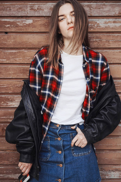 Portrait of a woman in rock, grunge style. Filmed on the street, in the open space. Dressed in a black leather jacket, shirt in red plaid. Street style and fashion. - Photo, Image