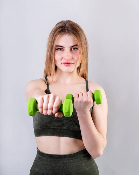 Sport und Fitness. Junge sportliche Frau macht Übungen mit Hanteln isoliert auf grau - Foto, Bild