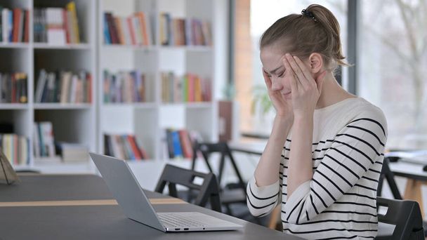 Uso de laptop por mulher jovem com dor de cabeça na biblioteca
 - Foto, Imagem