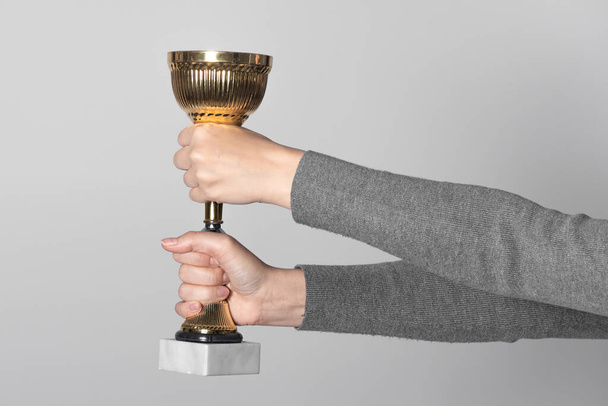 Golden award cup in winner hand isolated on gray background. Award ceremony. - Foto, afbeelding