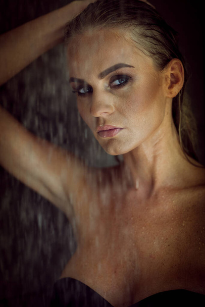 Relaxation and spa concept. Portrait of a sexy fashionable lady in a black swimsuit. Woman with wet hair and makeup poses in shower near swimming pool in natural light - Foto, Bild