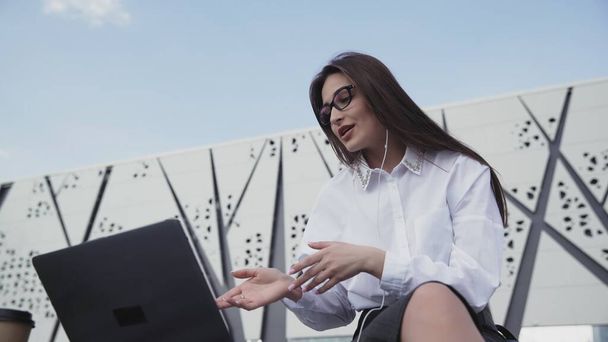 Mladá kavkazská obchodní žena s dlouhými vlasy mluvit na skype pomocí notebooku sedí venku. - Fotografie, Obrázek