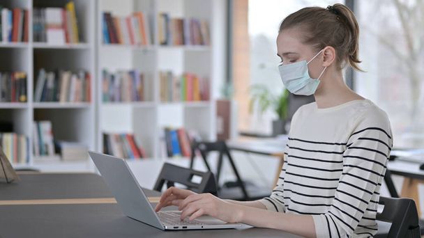 Young Woman with Face Mask using Laptop in Library - Fotografie, Obrázek