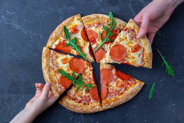 Family snack, mother and child hands taking pepperoni pizza slices. Italian traditional lunch or dinner. Fast food and street food concept. Flat lay, top view, close up - Photo, image