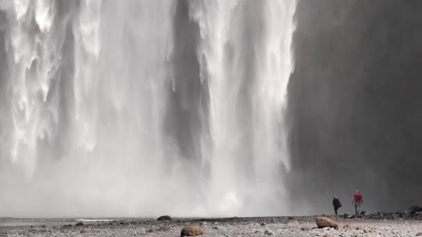 Hombre y mujer caminando bajo la cascada Skogafoss Islandia cámara lenta
 - Imágenes, Vídeo