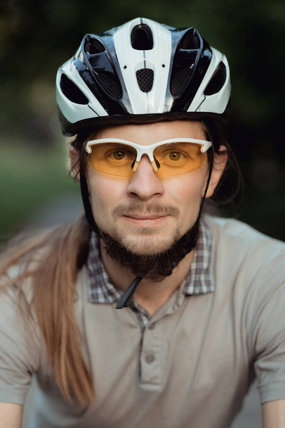 Retrato del hombre con gafas de sol amarillas y casco de pie con bicicleta en la carretera y mirando a la cámara
 - Foto, imagen