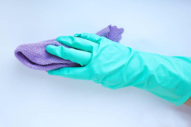 χέρι σε ένα μπλε λαστιχένιο γάντι με μωβ πετσέτα σε λευκό φόντο. έννοια καθαρισμού. - Φωτογραφία, εικόνα