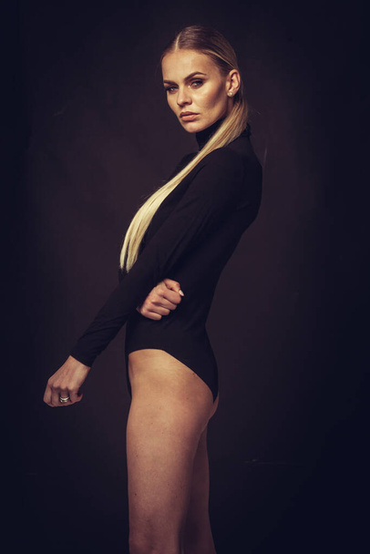 Mode- und Dessouskonzept - schönes blondes Damenporträt in sexy schwarzem Rollkragenkorsett auf dunklem Hintergrund. Frau in Unterwäsche posiert im Studiolicht - Foto, Bild