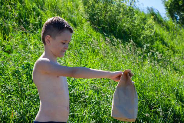 the boy holds out a paper bag. nature. delivery. we will clean up the nature behind us - Фото, изображение