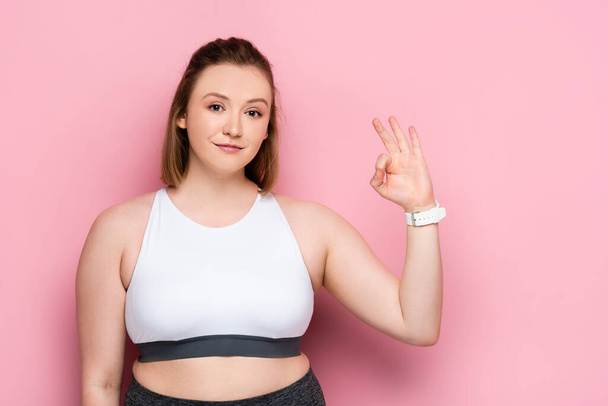 Lächelndes übergewichtiges Mädchen zeigt okay Geste auf rosa - Foto, Bild