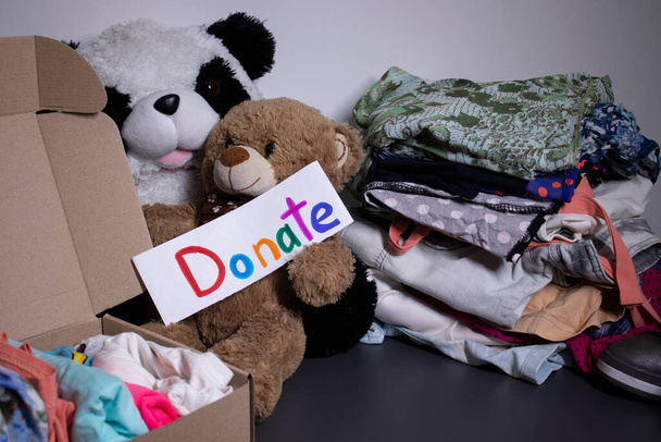 Spendenschild handgeschrieben mit bunten Buchstaben. Eine Schachtel mit Kleidung und ein Stapel Kleider in der Nähe auf einem grauen Tisch. Kopierraum - Foto, Bild