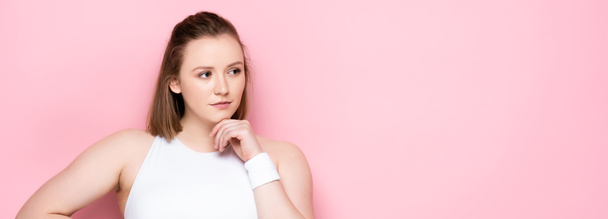 horizontal image of pensive overweight girl touching chin and looking away on pink - Photo, Image