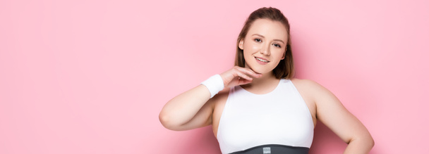 panoramic shot of pretty overweight girl touching chin and looking at camera on pink - Foto, afbeelding