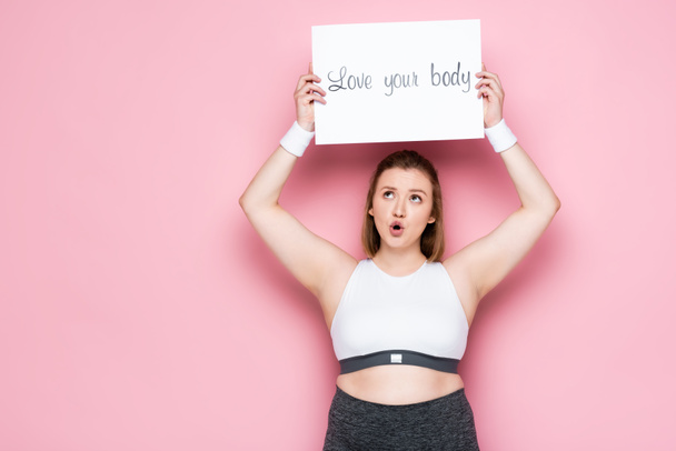 excited overweight girl holding placard with love your body inscription above head on pink  - 写真・画像