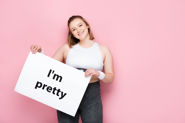 χαρούμενο υπέρβαρο κορίτσι κρατώντας πλακάτ με Είμαι όμορφη επιγραφή στο ροζ  - Φωτογραφία, εικόνα