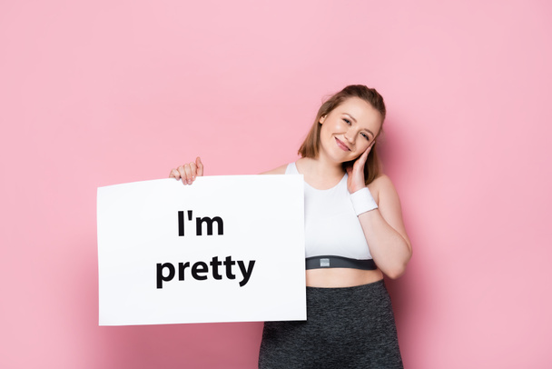 smiling overweight girl holding placard with i am pretty inscription on pink  - Fotoğraf, Görsel