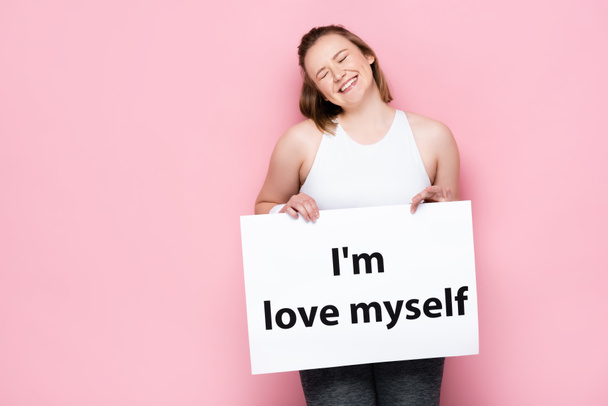 alegre chica con sobrepeso con los ojos cerrados sosteniendo pancarta con me amo inscripción en rosa
  - Foto, Imagen