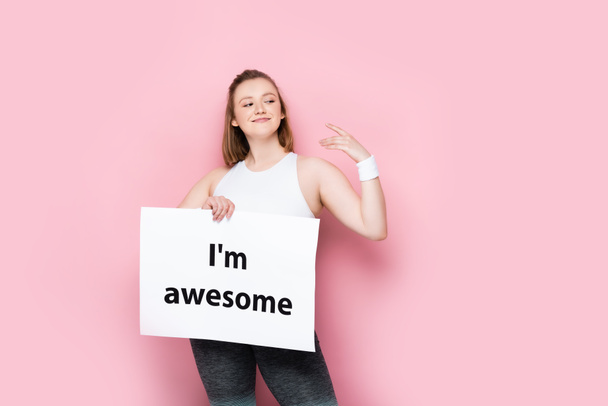 happy overweight girl holding placard with i am awesome inscription on pink - Photo, Image