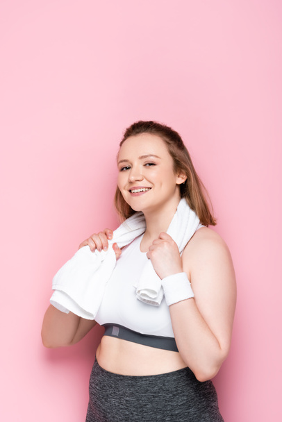 glückliches übergewichtiges Mädchen wischt sich den Hals mit einem Handtuch ab und lächelt in die Kamera auf rosa - Foto, Bild