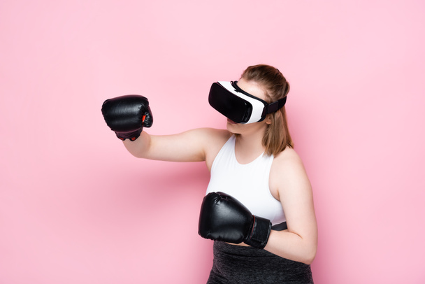 συν μέγεθος κορίτσι σε vr ακουστικά και γάντια πυγμαχίας μιμείται αγωνίζονται σε ροζ - Φωτογραφία, εικόνα