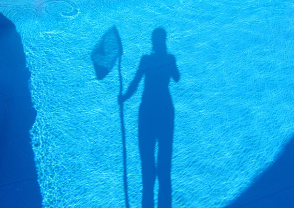 Silhouette eines Mädchens mit einem Schmetterlingsnetz. Reinigung des schmutzigen leeren Pools von Algen, Wassersteinen und Kalk. Beginn der Badesaison im heißen Sommer. - Foto, Bild