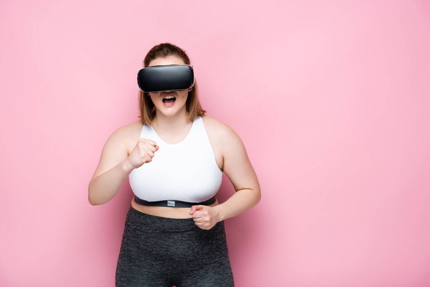 angry overweight girl in sportswear and vr headset with clenched fists on pink - Foto, Imagem