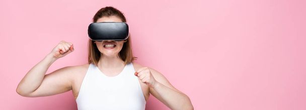 horizontal image of aggressive overweight girl in sportswear and vr headset with clenched fists on pink - Valokuva, kuva