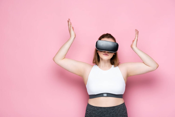 confused size plus girl in vr headset and sportswear showing shrug gesture on pink - Fotó, kép