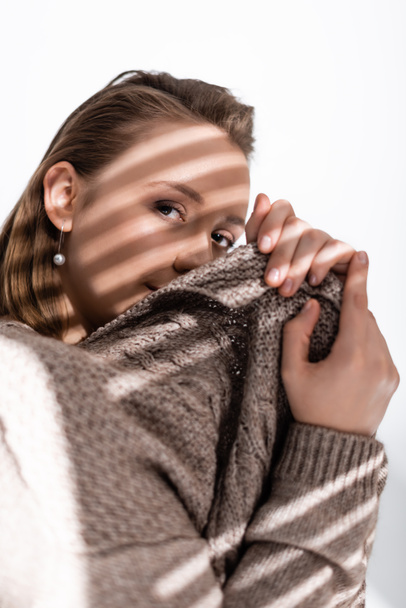 attractive overweight girl obscuring face with grey sweater and looking at camera on white with sunlight and shadows - Foto, imagen