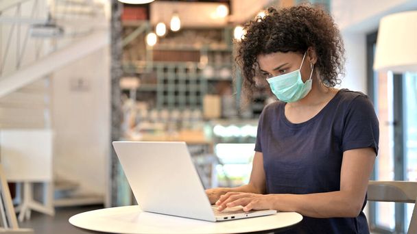 African Woman with Face Mask Working on Laptop in Cafe - 写真・画像