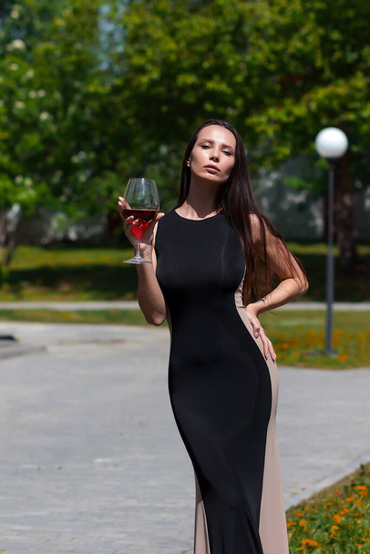 魅力的な女性で黒エレガントなドレスは首に触れ、公園で晴れた夏の日に赤ワインを楽しむ - 写真・画像