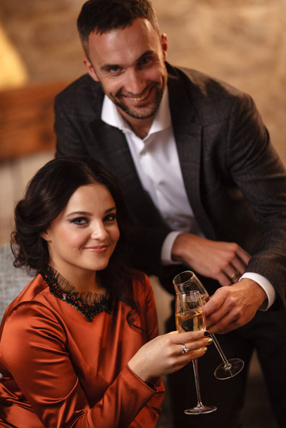 Romance and dating concept. Young couple man and woman with champagne glasses celebrating and toasting in restaurant. Two people male and female in elegant evening suit and dress on romantic dinner - Fotografie, Obrázek