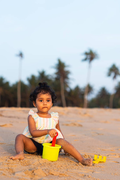  Jolie fille indienne ludique enfant / nourrisson sur le côté de la plage jouant avec un kit de sable et donnant des expressions joyeuses.  - Photo, image