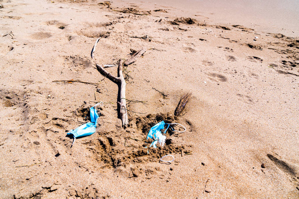 Máscaras médicas usadas e jogadas na areia de uma praia vazia. Contaminação por coronavírus vívido
. - Foto, Imagem