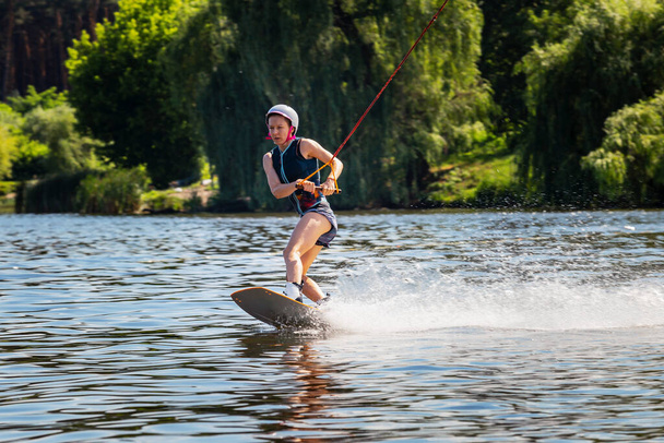 Donna in sella al wakeboard. Taglia onde e solleva spruzzi in un lago estivo - Foto, immagini