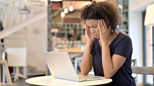 カフェでノートパソコンを使って頭痛を持つ若いアフリカ人女性 - 写真・画像