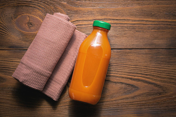 Carrot juice in a bottle and kitchen towel on wooden table background. - Foto, Imagem