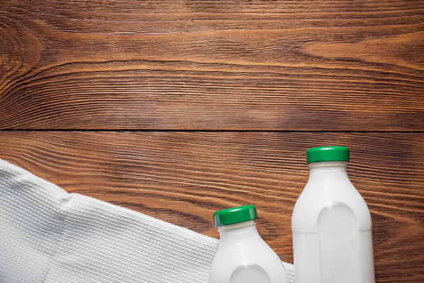 Bottle of fresh milk and kitchen towel on brown wooden table background. - Photo, Image