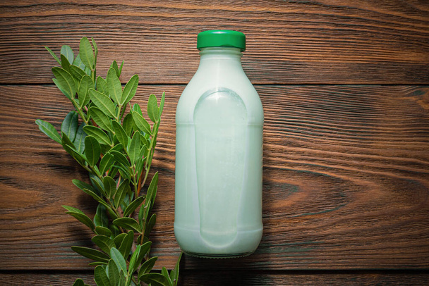 Pistachio milk in a bottle and green pistachio tree branch with green leaves on wooden table background. - Photo, Image