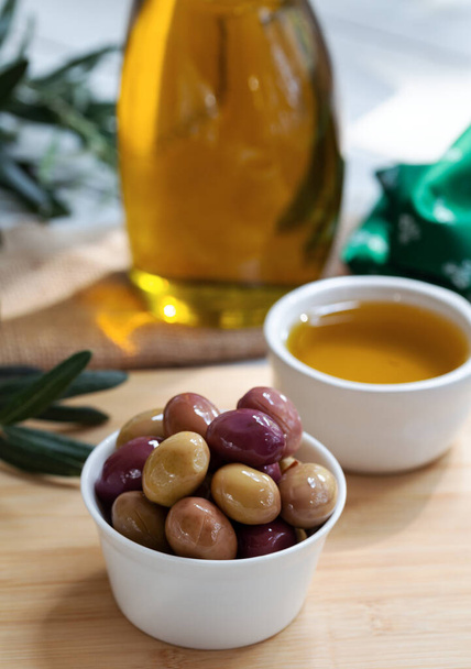 Black and green olives and oil in bowl on wooden background. - Fotografie, Obrázek