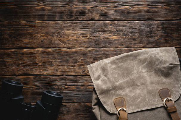 Travel or adventure flat lay background with copy space. A backpack and a binoculars on a brown wooden table. - 写真・画像