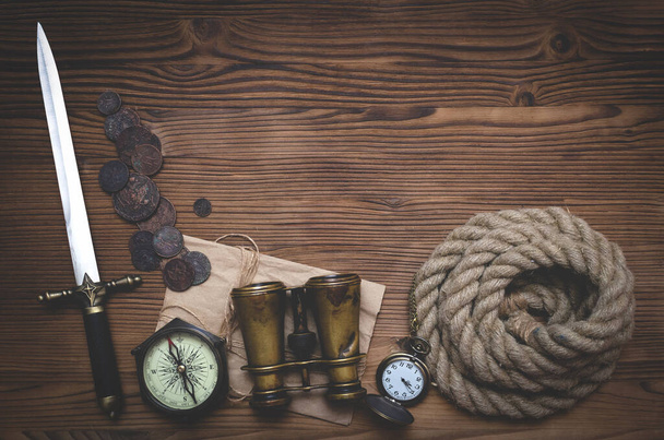 Travel or adventure flat lay background with copy space. Adventurer table. Binoculars, pocket watch, coins, old parchment, moorings, compass and pocket watch on the table. - Photo, Image