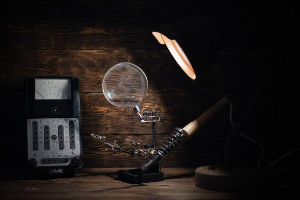 Retro analog voltmeter and soldering iron in the light of lamp on a brown wooden table background. Electrical works abstract background.  - Φωτογραφία, εικόνα