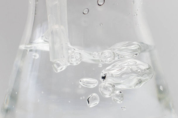 Closeup of a liquid with bubbles in a glass erlenmeyer flask with a plastic pipette in it on a white background. Science experiment. - Photo, Image