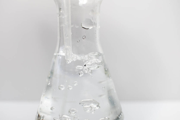 Gros plan d'une fiole Erlenmeyer en verre avec une pipette en plastique dedans avec des bulles dans le liquide sur un fond blanc. Sciences. - Photo, image