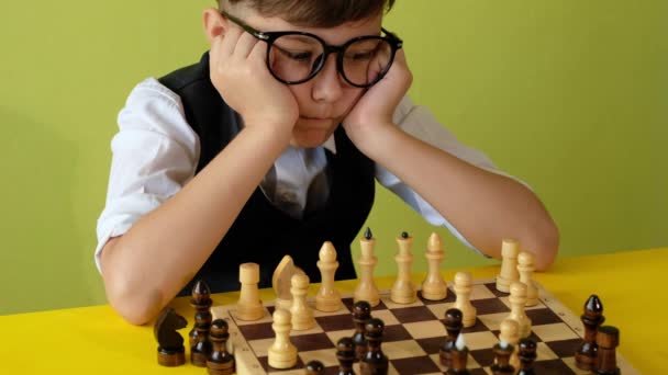 Niño jugando al ajedrez en la mesa. Niño con gafas desarrollando estrategia de ajedrez, jugar juego de mesa con un amigo. - Metraje, vídeo