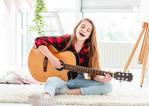 Pretty girl playing guitar sitting on floor - Фото, изображение