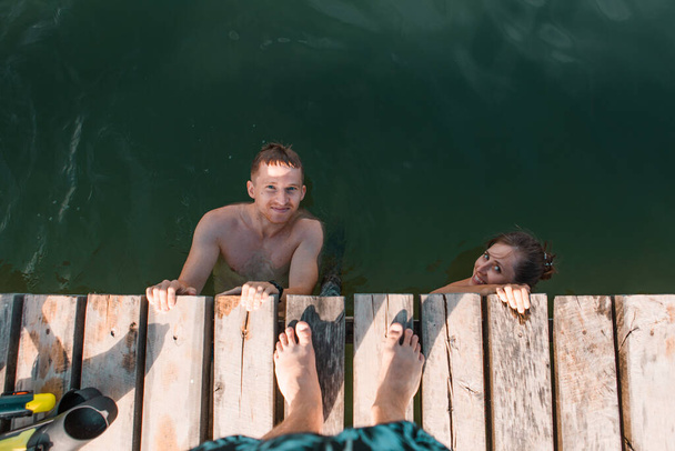 vista di coppia in acqua dal molo di legno. attività estive. copia spazio - Foto, immagini